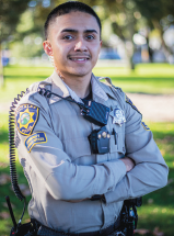 Police Officer Fierros in uniform standing at park with arms crossed, smiling